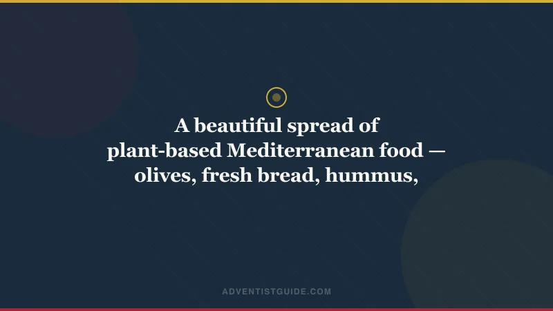 A beautiful spread of plant-based Mediterranean food — olives, fresh bread, hummus, grapes, vegetables — on a rustic table in warm light